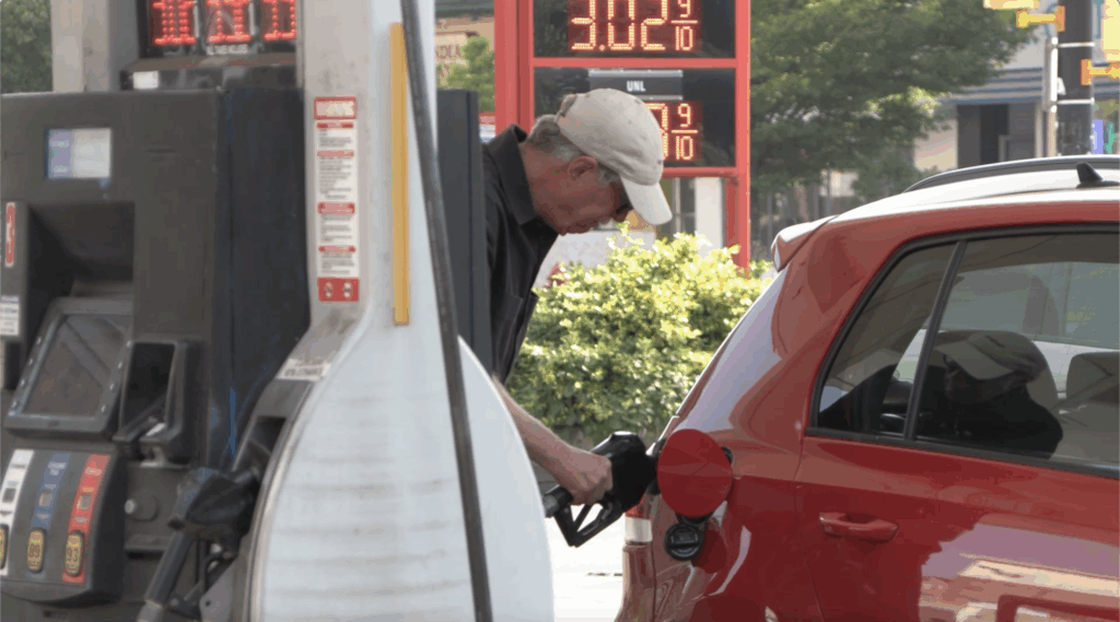 A man manually fuels his car at a gas station.